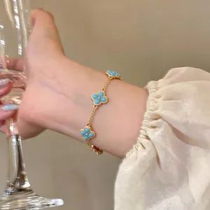 Detailansicht eines vergoldeten Armbands mit türkisfarbenen Kleeblatt-Anhängern.