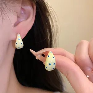 Close-up of C-shaped drop oil earrings in light yellow with blue polka dots pattern