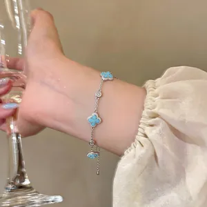 Nahaufnahme eines silbernen Armbands mit türkisfarbenen Kleeblatt-Anhängern am Handgelenk.