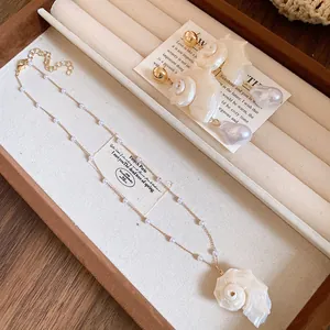 Detail view of a seashell pendant necklace and matching baroque pearl earrings on a tray.