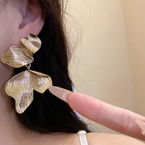 Detailed view of large gold leaf earrings with intricate textures and silver needle