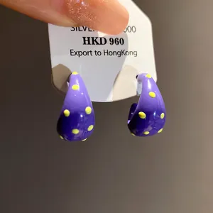 Close-up detail of vibrant purple C-shaped enamel hoop earrings with yellow polka dots