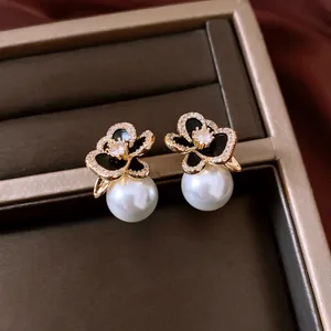 Detailed macro shot of floral gold earrings with cubic zirconia and white pearl drop