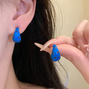 Detailed close-up view of blue C-shaped drip oil earrings with red polka dot patterns