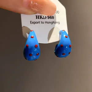 Detailed macro view of blue C-shaped hoop earrings with vibrant red polka dots