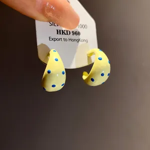 Close-up of yellow C-shaped enamel hoop earrings with blue polka dot pattern detail