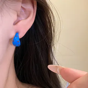 Close-up of blue C-shaped oil-drip earrings with red polka dots on an ear.