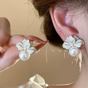 Close-up of elegant French style white enamel flower earrings with a luminous pearl drop
