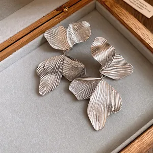 Macro shot of silver dangling earrings with realistic leaf texture inside a wooden box