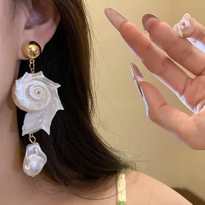Close-up view of a unique conch shell and baroque pearl earring worn by a model for fashion
