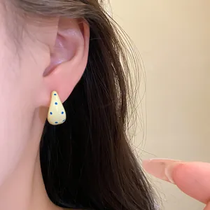 Close-up view of elegant yellow C-shaped oil-drip stud earrings with blue polka dots