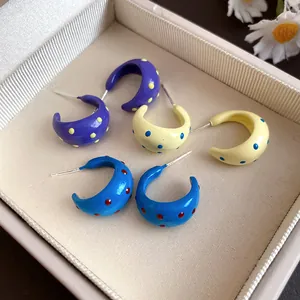 Close-up of vibrant colorful C-shaped stud earrings with polka dot patterns in a box.