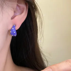 Close-up of purple C-shaped stud earring with yellow polka dots on model's ear.