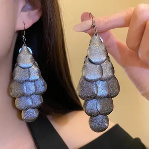 Detailed close-up view of large silver glitter waterdrop tassel earrings worn on model