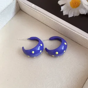 Detail view showing blue enamel C-shaped stud earrings with charming yellow polka dots