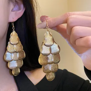 Detail view of matte gold water-drop tassel earrings with a textured scale design
