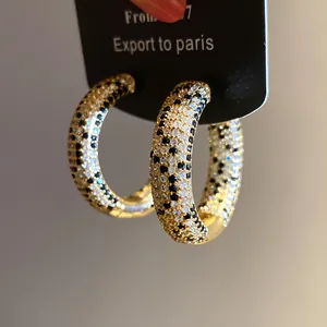 Dettaglio di orecchini a cerchio placcati oro 18k con eleganti zirconi neri e bianchi