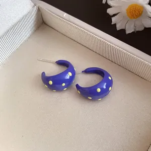 Close-up of purple C-shape enamel hoop earrings with yellow polka dots on a gift box