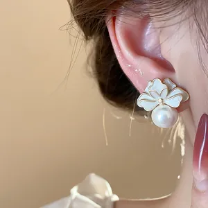 Close-up of elegant French style white enamel flower stud earrings with pearl pendant