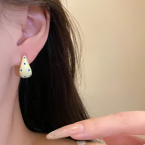 Detailed close-up of yellow C-shaped drip oil stud earrings with blue polka dots on model's ear