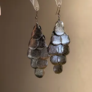 Macro detail of matte metallic teardrop tassel earrings with multi-layered scales
