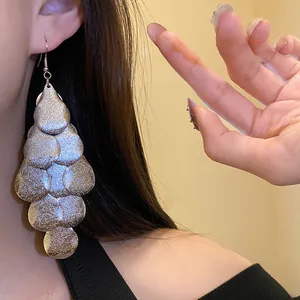 Detailed close-up of metallic matte teardrop fringe earrings worn by a model