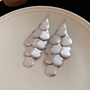 Detailed view of silver matte layered teardrop tassel earrings on a textured plate