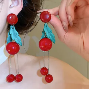 Detailed macro view of vibrant red cherry earrings with green leaves and silver tassels