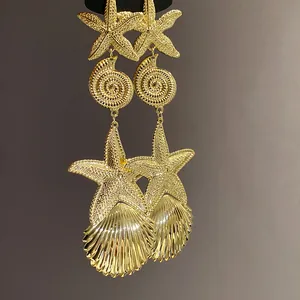 Nahaufnahme goldener Metallohrringe mit Seestern-, Seeschnecken- und Muschelmotiven.