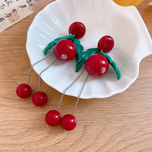 Close-up detail of sweet red cherry tassel earrings with green leaf accents on shell
