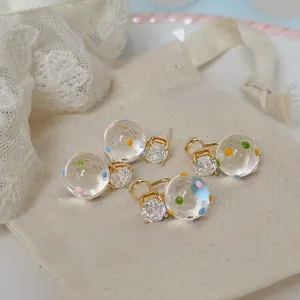 Dettaglio di orecchini a lobo placcati oro 18k con pois colorati e zirconi.