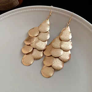 Detail shot of matte gold layered teardrop tassel earrings on a white ceramic plate