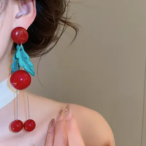 Detail of red cherry dangle earrings with green leaves on a model's ear