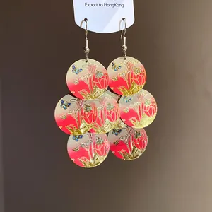 Close-up of elegant drop earrings with floral and butterfly prints on circular metal discs