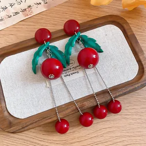 Detailed view of red cherry earrings with green leaves and long silver tassels