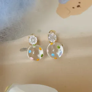 Dettaglio di orecchini in zircone placcati oro 18k con pois colorati in resina trasparente.
