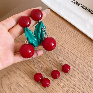 Close-up view of elegant red cherry drop earrings with green leaves and bead tassels