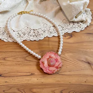 Elegant pearl necklace with a pink camellia flower pendant on a rustic wooden background