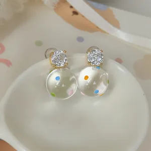 Dettaglio ravvicinato di orecchini a sfera trasparenti con pois colorati e zirconi lucenti.
