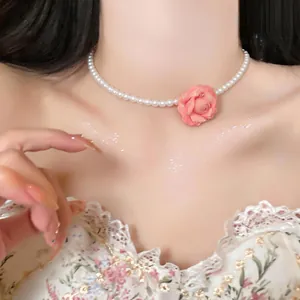 Close-up detail of a sweet pink rose flower and white pearl necklace on a female neck.