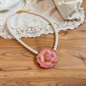 Elegant close-up of pink camellia pendant pearl necklace on a vintage lace background