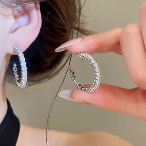 Detailed macro shot of sparkling silver C-shaped zircon hoop earrings on a model.
