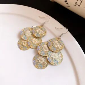 Close-up detail of gold dangle earrings featuring a blue and white floral oil print.
