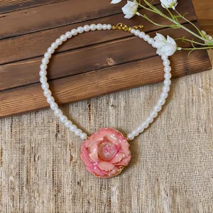 Macro view of elegant pink flower pendant with white pearls on rustic wooden background