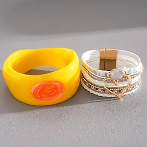 Close-up detail view of bold yellow resin bangle and multi-layer white leather heart bracelet