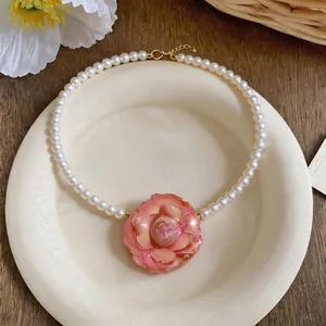 Detail of an elegant white pearl necklace with a pink camellia flower pendant on a ceramic plate
