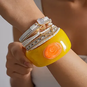 Close-up view of a layered white leather heart bracelet and chunky yellow resin bangle.
