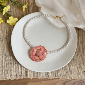 Close-up of elegant pearl necklace with a large pink flower pendant on a white plate