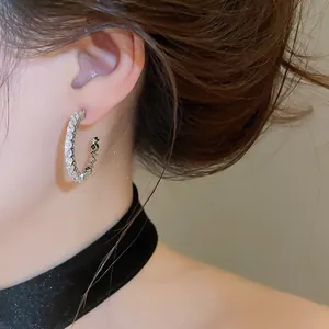 Detail view showing sparkling cubic zirconia stones on silver C-hoop earrings worn by model.