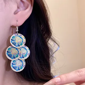 Close-up detail of bohemian blue and gold enamel floral drop earrings worn by a model
